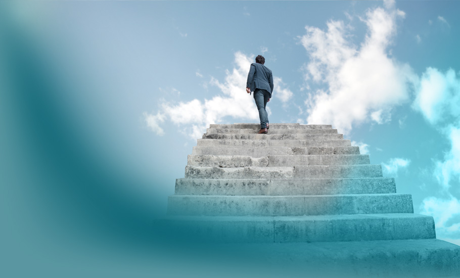 Aufgabe einer Führungskraft: Ein aufstrebender Businessmann auf einer monumentalen Treppe vor blauem Himmel - metaphorisch für Karrierewachstum und Zielsetzung.